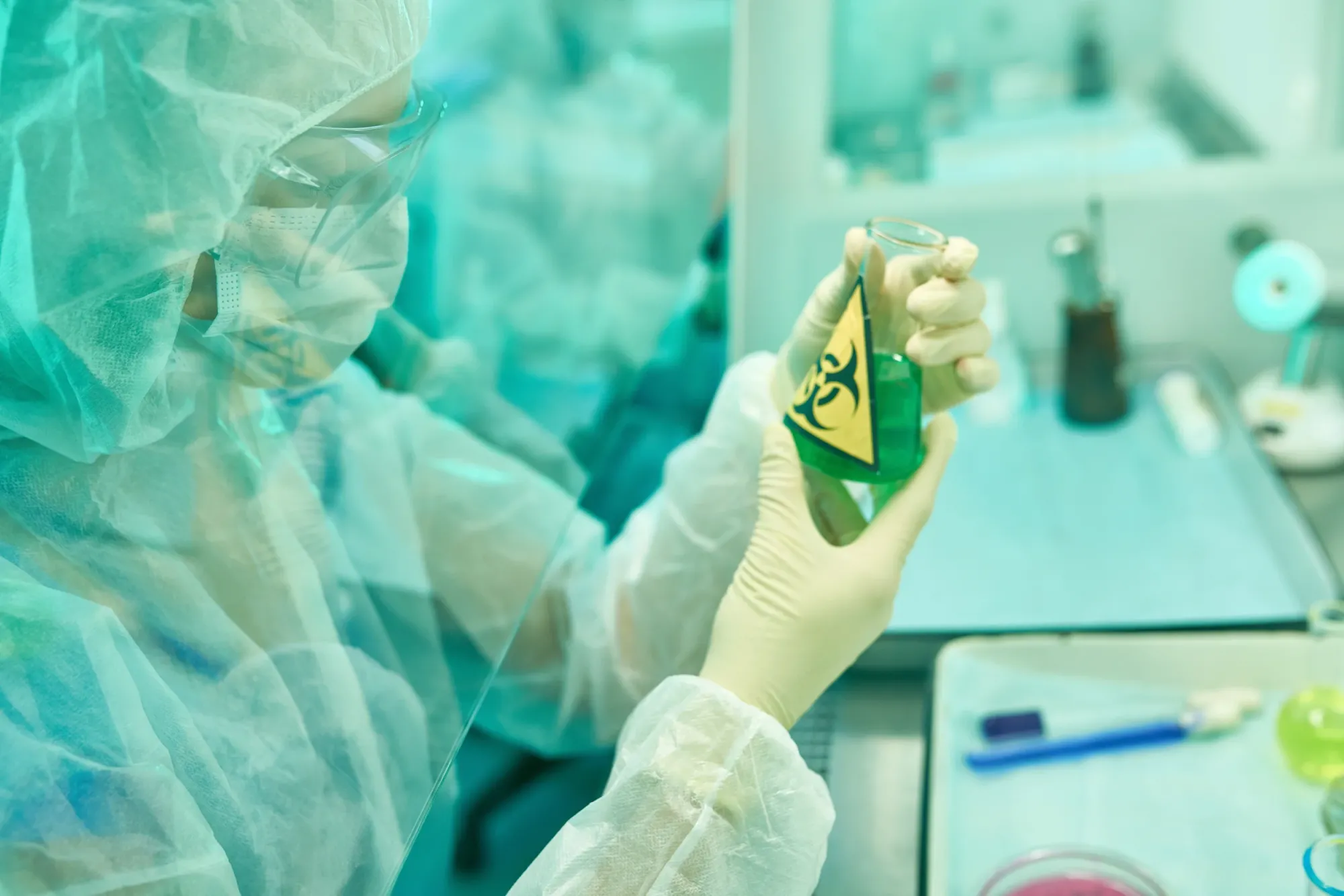 Person wearing personal protective equipment holding a beaker marked with the biohazard symbol