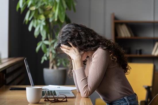 Woman with her head in her hands sitting at a desk with a laptop.